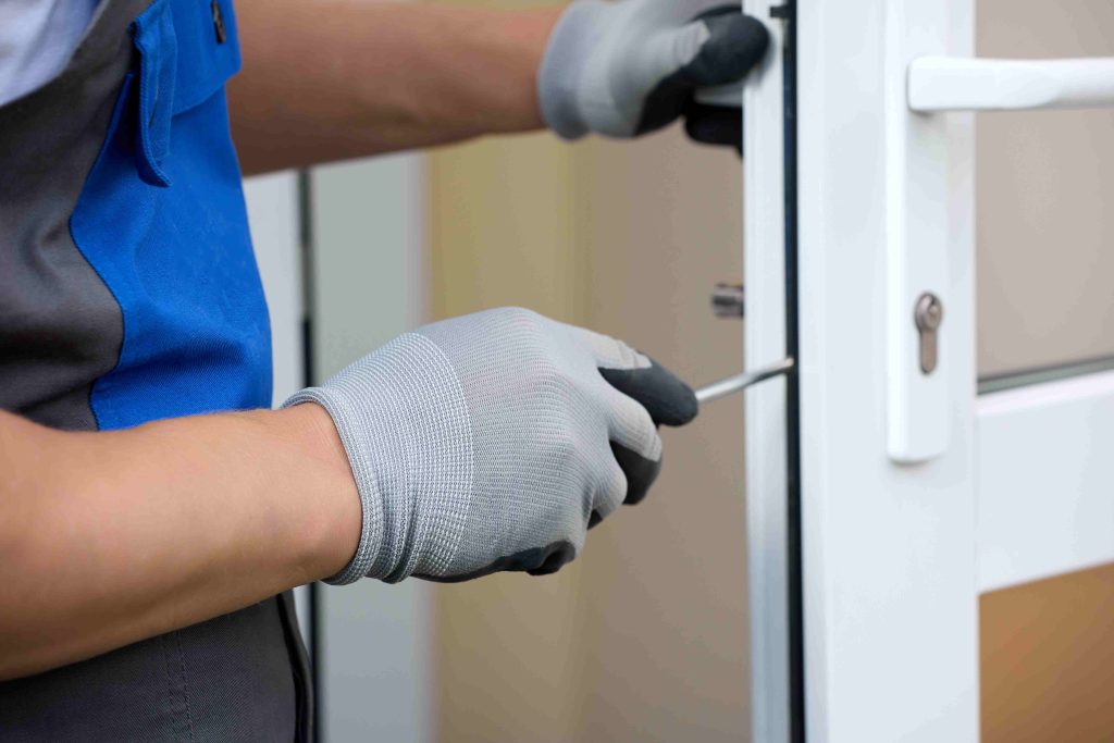 closeup man working with gloves with screwdriver repairing lock plastic door service maintenance repair plastic doors locks compressed